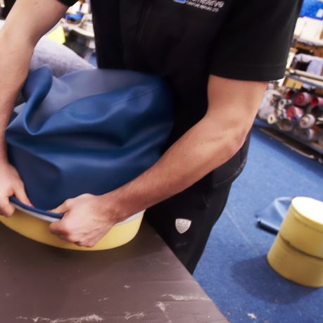 Furniture technician re-covering a stool seat with a new blue leather cover